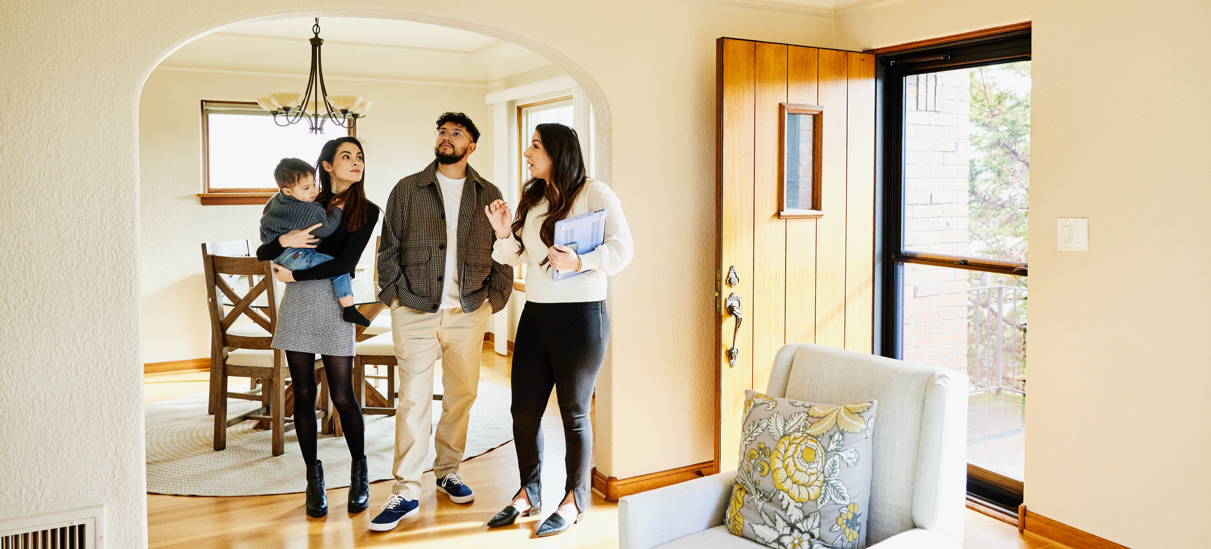 [Featured Image] A Realtor stands in a house with a young family.