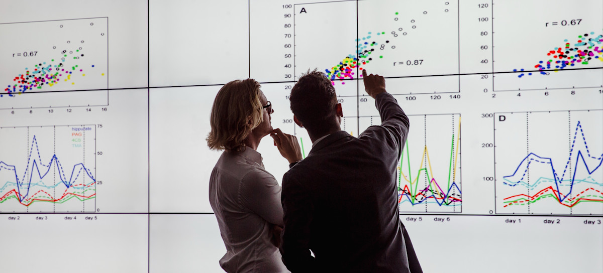 [Featured image] Two people stand in front of a monitor, viewing a data presentation built on fact and dimension tables.
