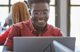 [Featured image] A young man in a red shirt and glasses studies for his double BA on his laptop. 