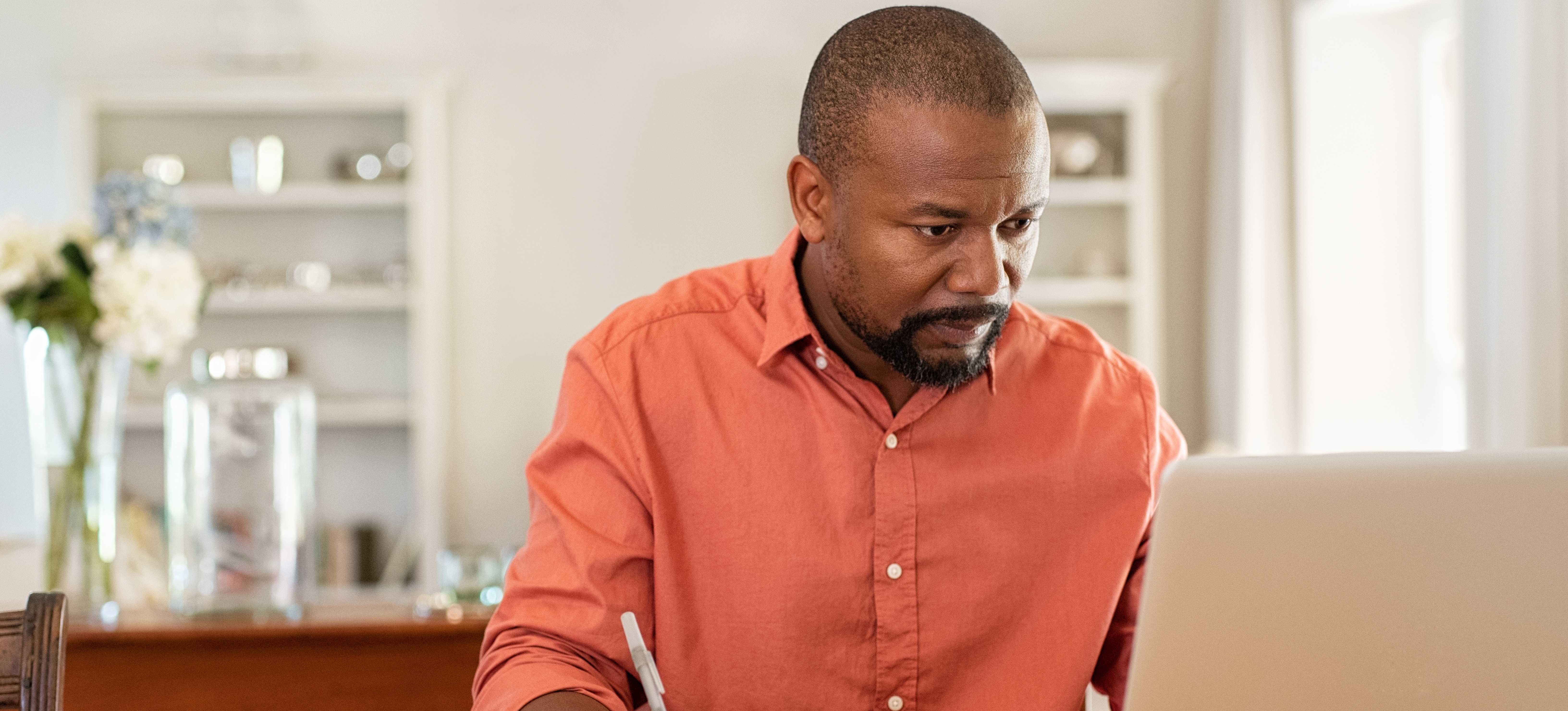 [Featured Image] A student sits at a desk with a laptop and notebook, studying for a postgraduate degree.
