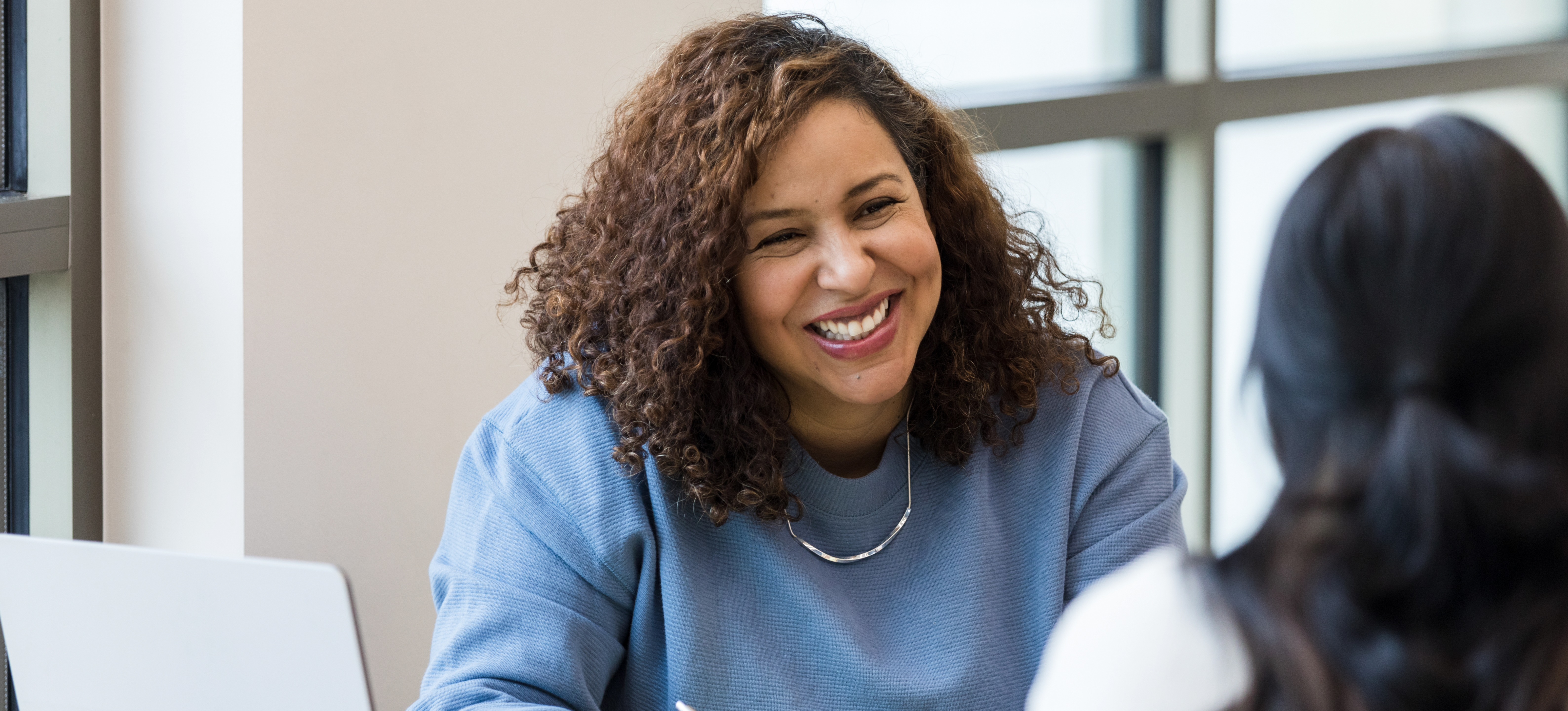 [Featured Image] A manager conducts a performance review meeting, smiling encouragingly while engaging in conversation with an employee in a professional setting.
