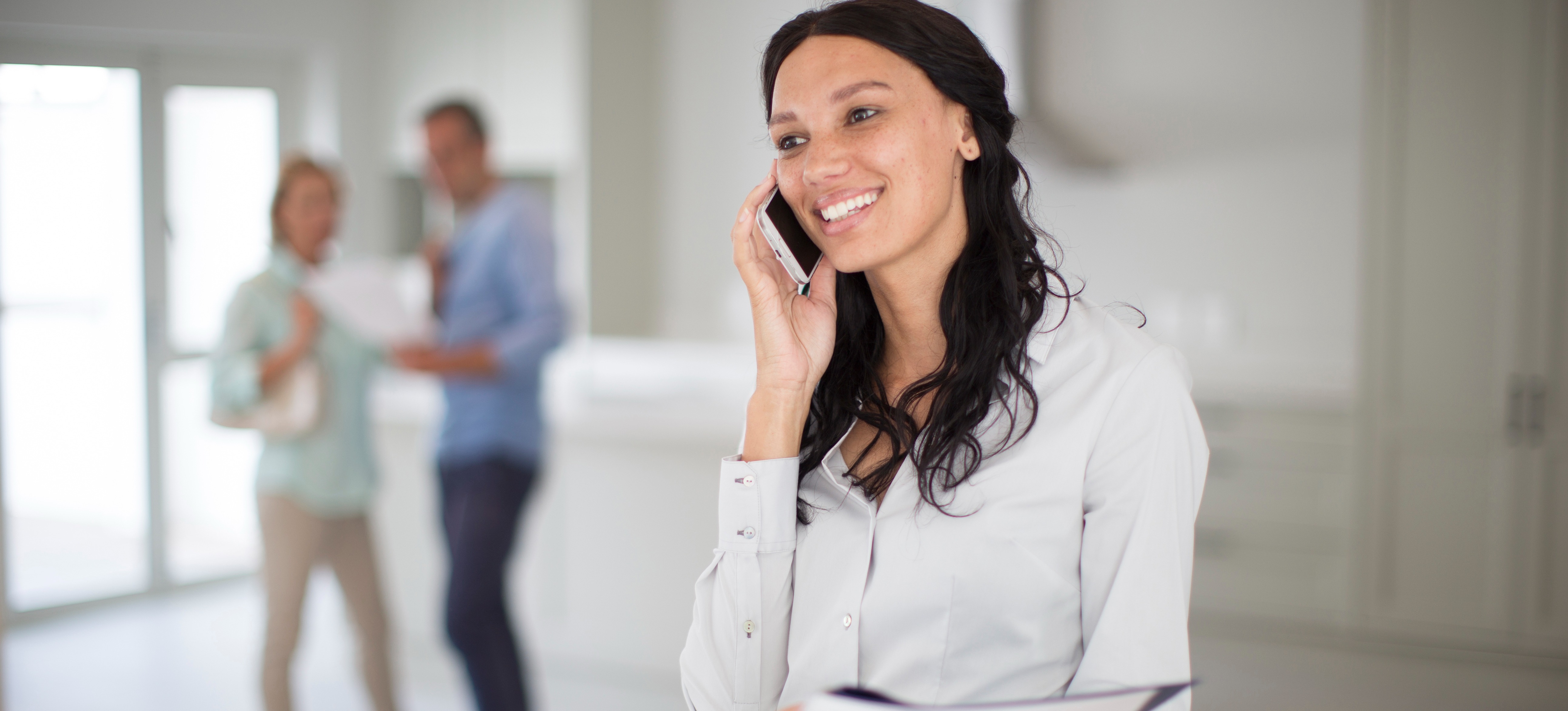 [Featured Image] A real estate agent, who found a job with an agency thanks to their impressive real estate agent resume, talks on the phone while showing a new home to a couple.
