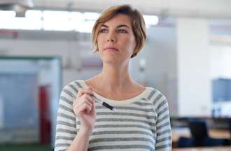 [Featured Image] A woman wearing a striped sweater is holding papers and a pen at an office. 