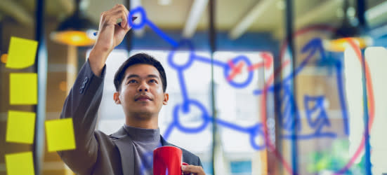 [Featured image] A scientist works towards their career goals while writing out formulas on a glass panel.