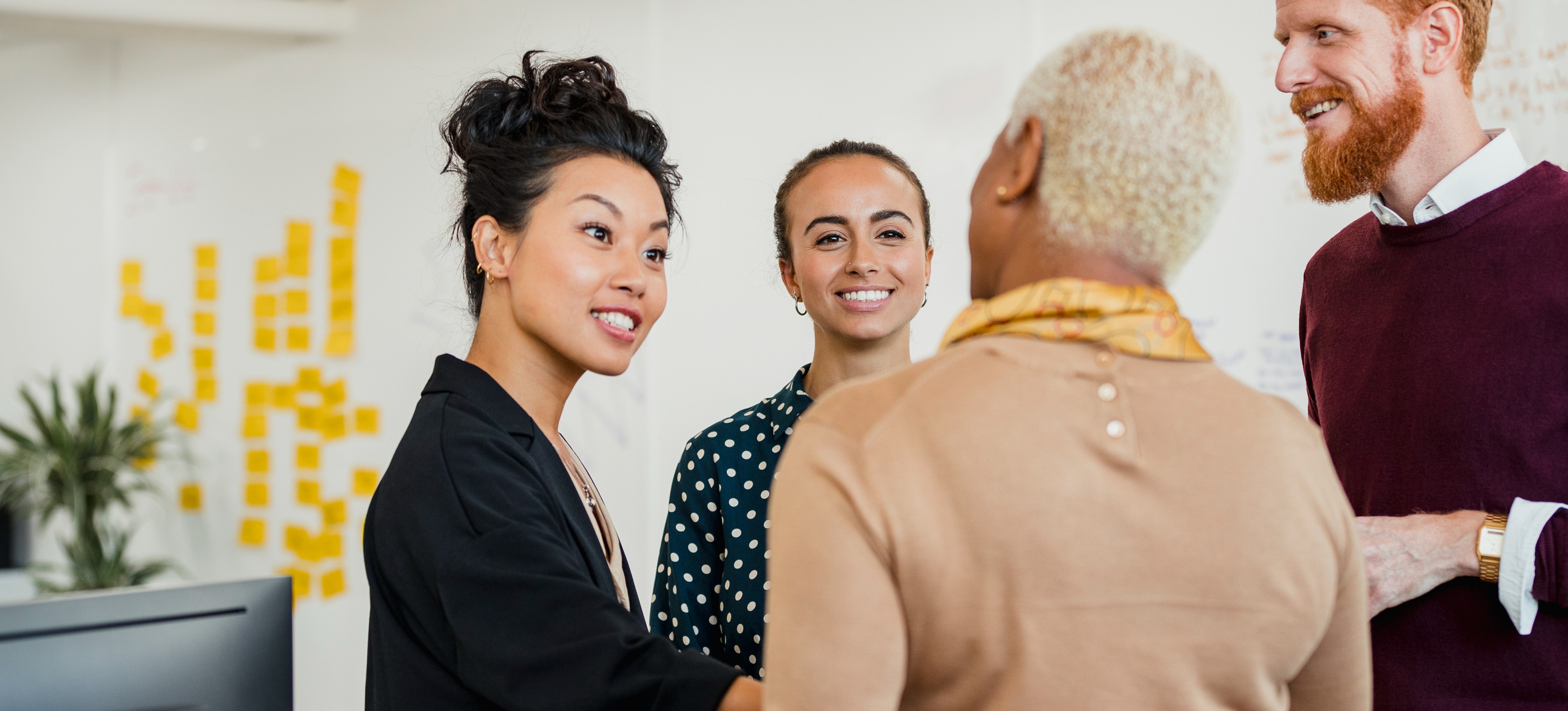 [Featured Image] A team of four, three women and one man, stand in their office and discuss Java project ideas.