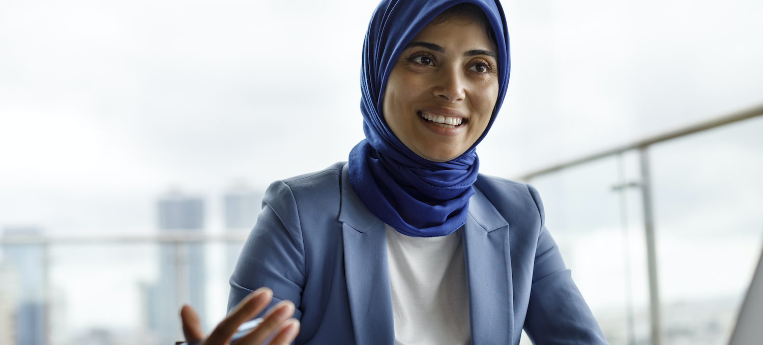 [Featured image] A social worker in a blue jacket with a scarf speaks with one of their patients in a brightly lit office.