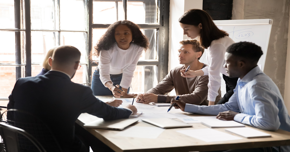 [Featured Image] A woman leads a team meeting in a conference room. 
