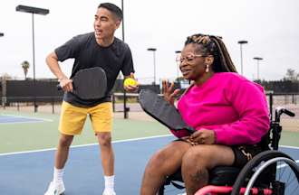 [Featured image] An exercise physiologist plays tennis with a client in a wheelchair.