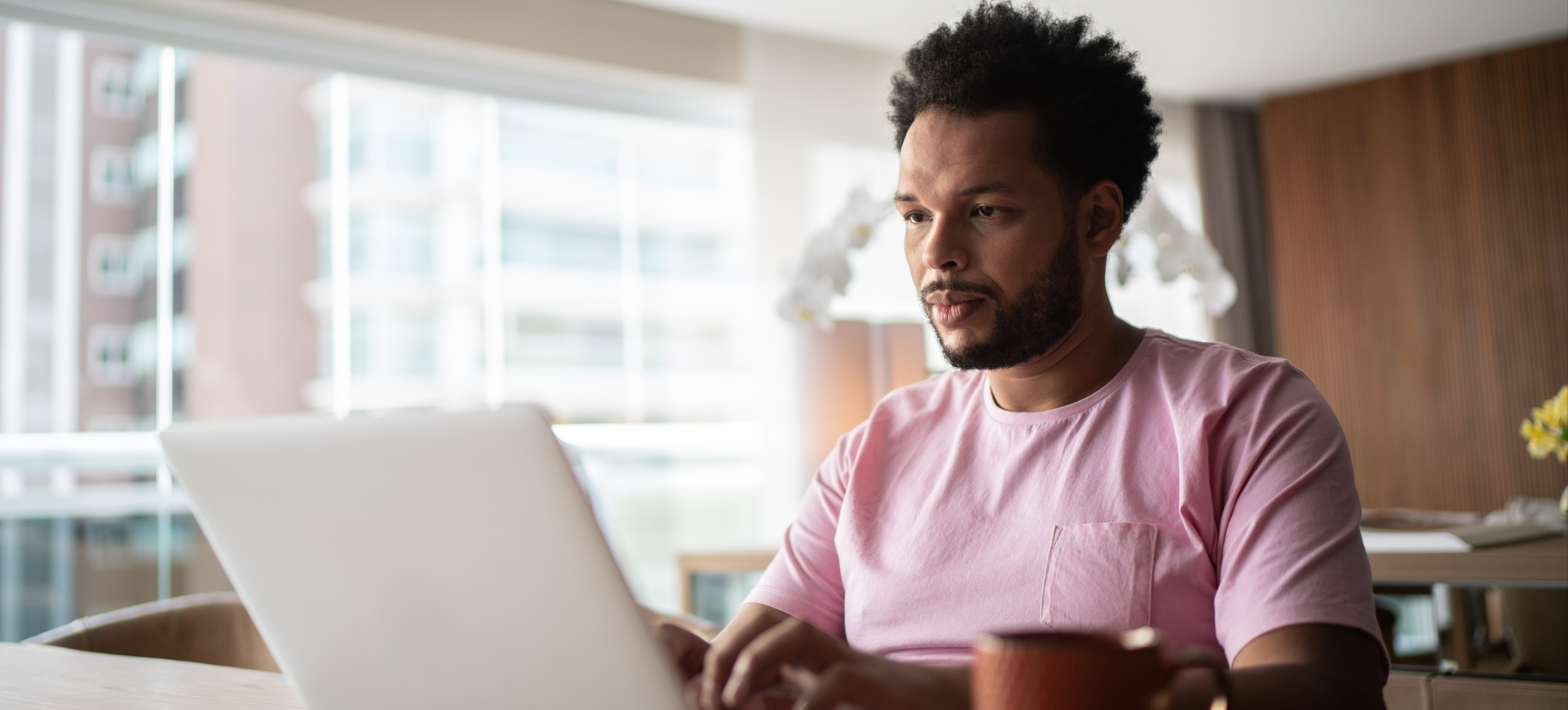 [Featured Image] A man sits at his laptop at home to research whether you need a degree to be a software engineer. 
