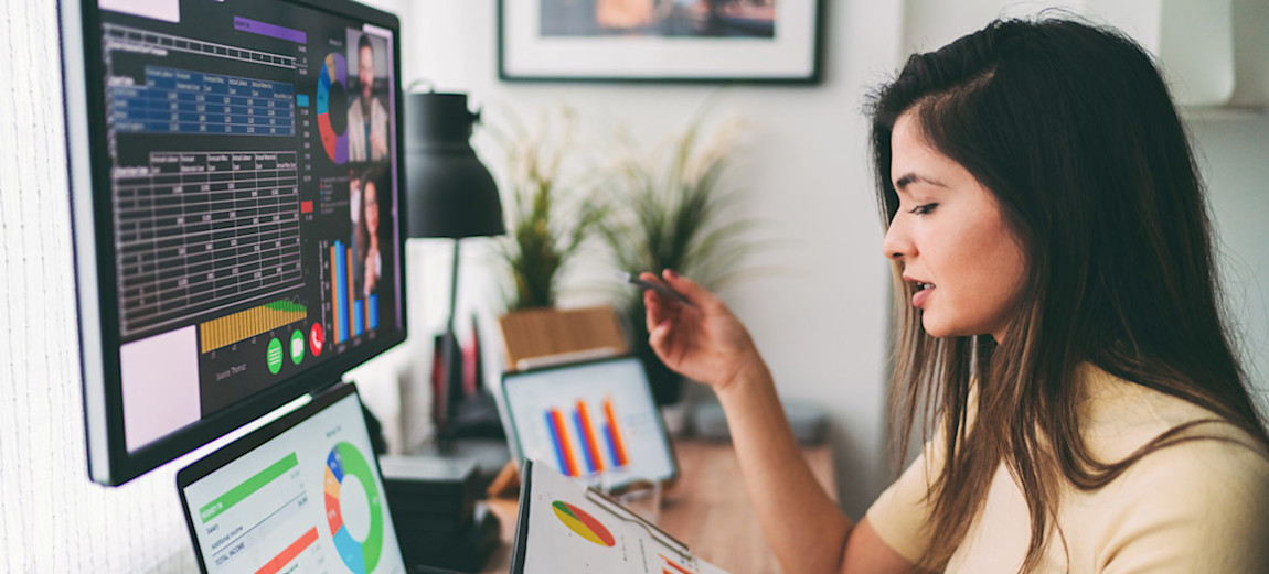 [Featured Image] A person working as a financial analyst salary sits at their multi-screen desktop computer and talks to two people over a video call as they look at graphs.
