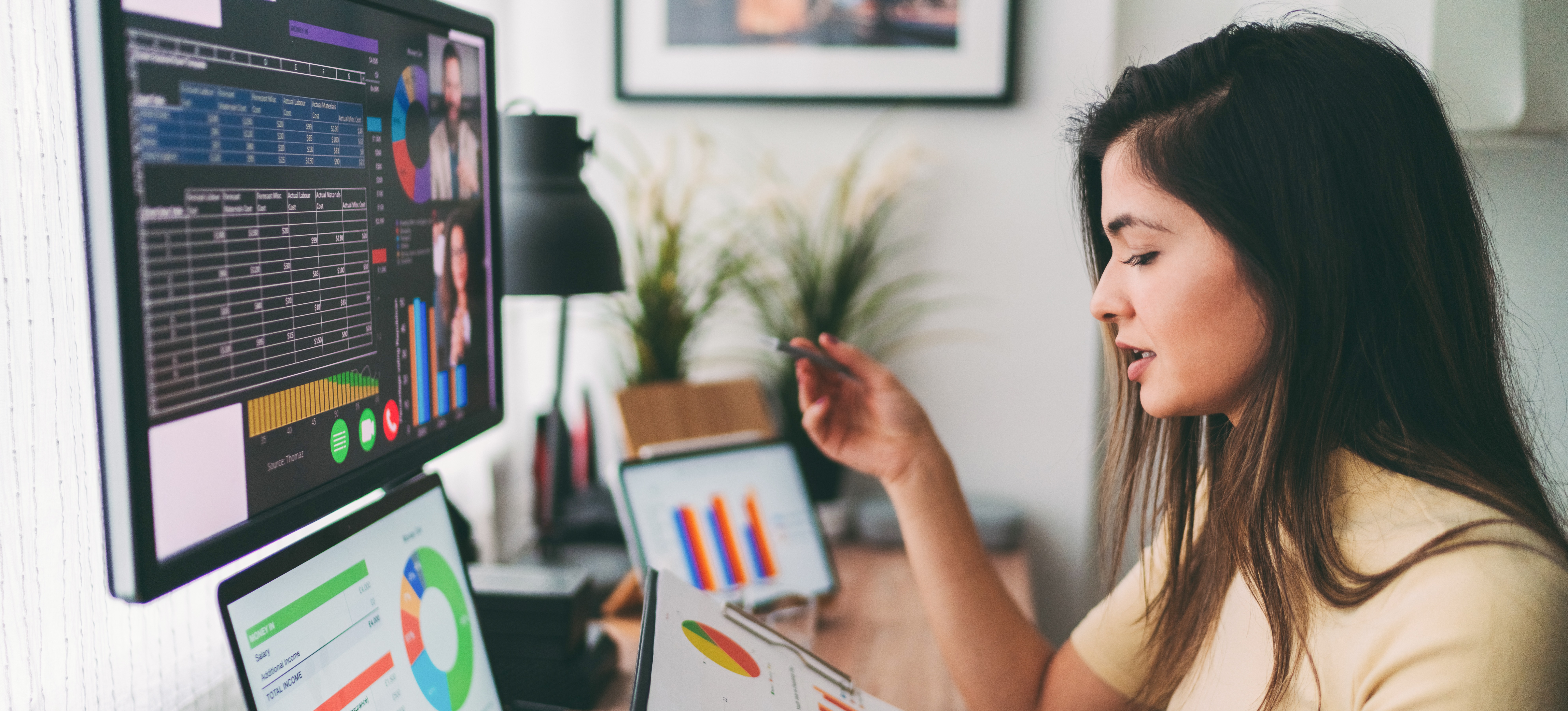 [Featured Image] A woman working as a financial analyst salary sits at her multi-screen desktop computer and talks to two people over a video call as she looks at graphs.
