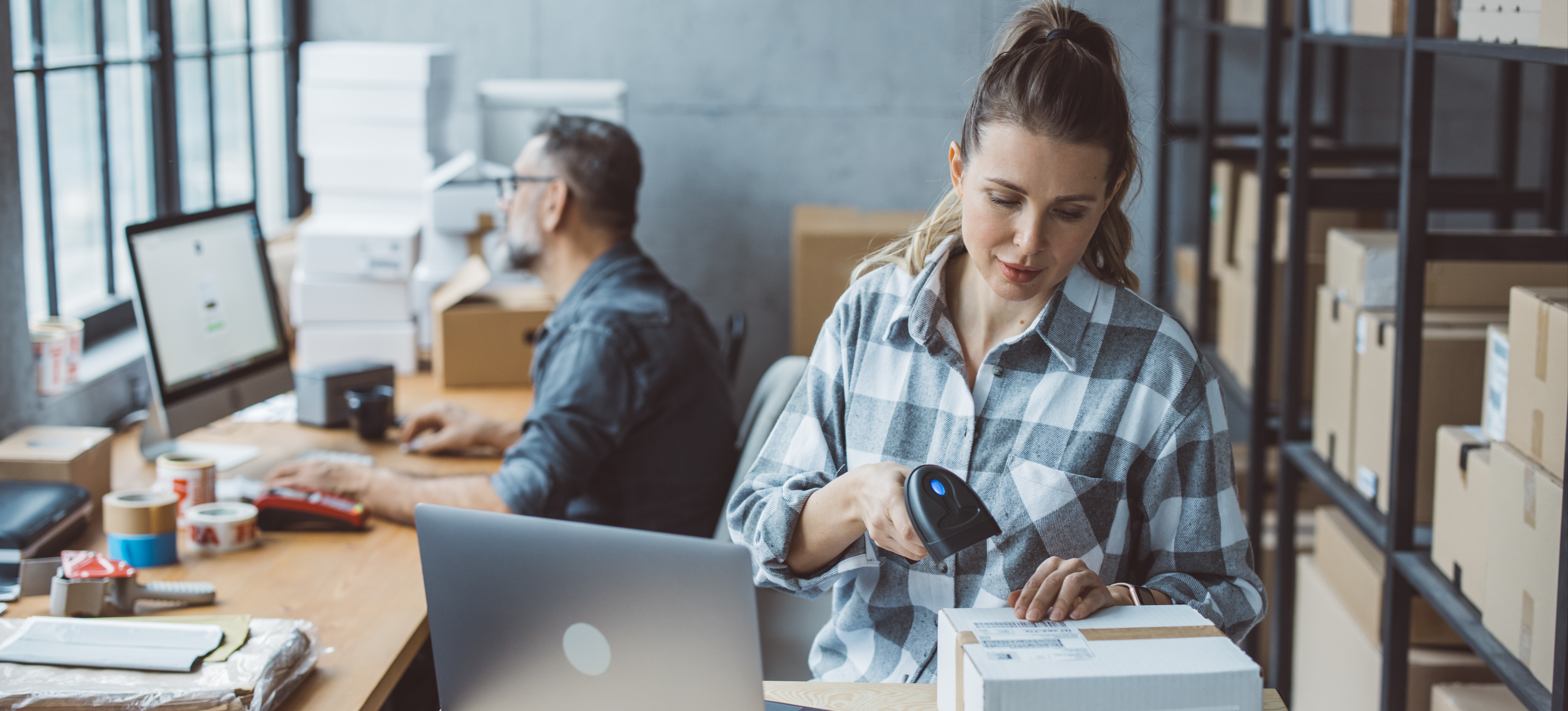 [Featured Image] A small business owner is packaging products to ship while her partner is researching competitive pricing for their new products.