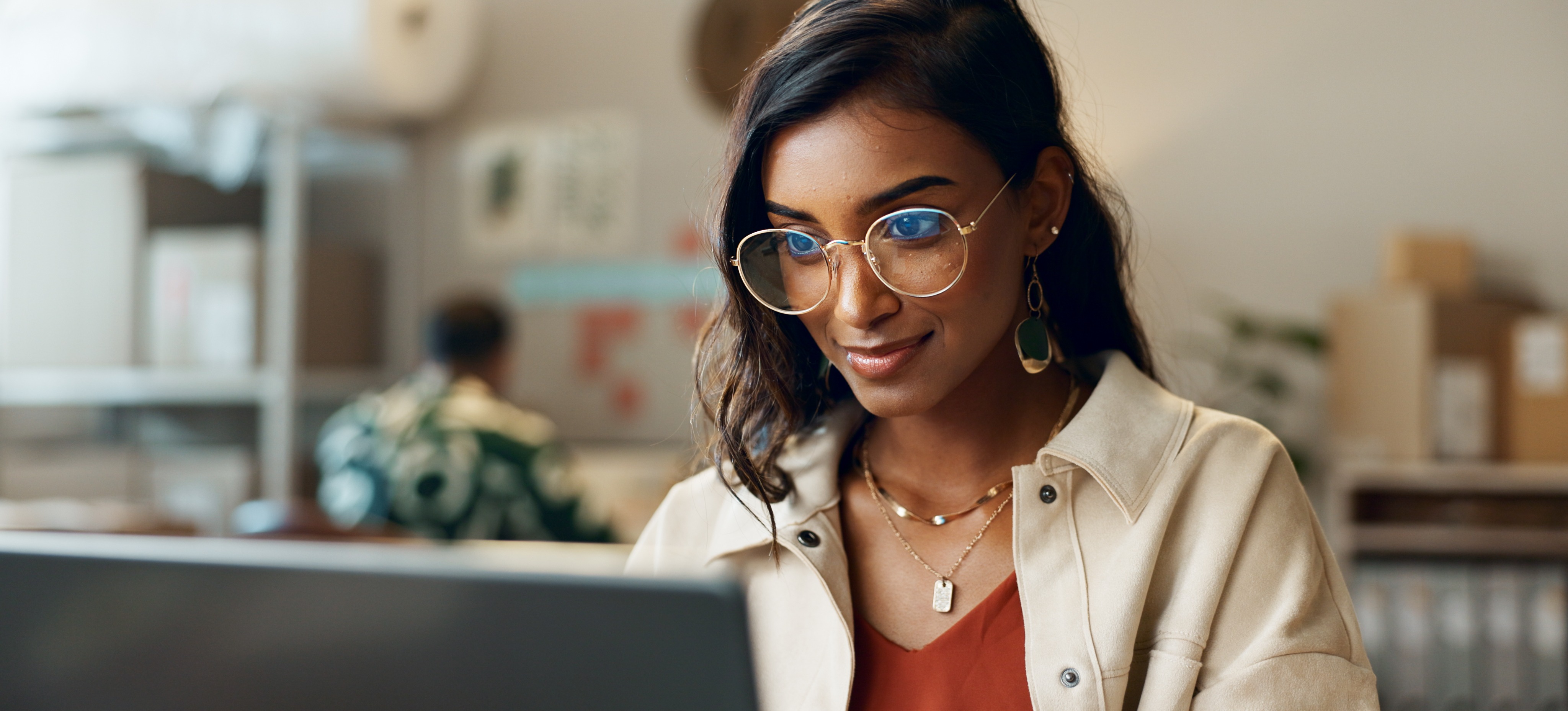 [Featured Image] A woman wearing glasses and looking at a laptop in front of her works on her supply chain analyst resume.
