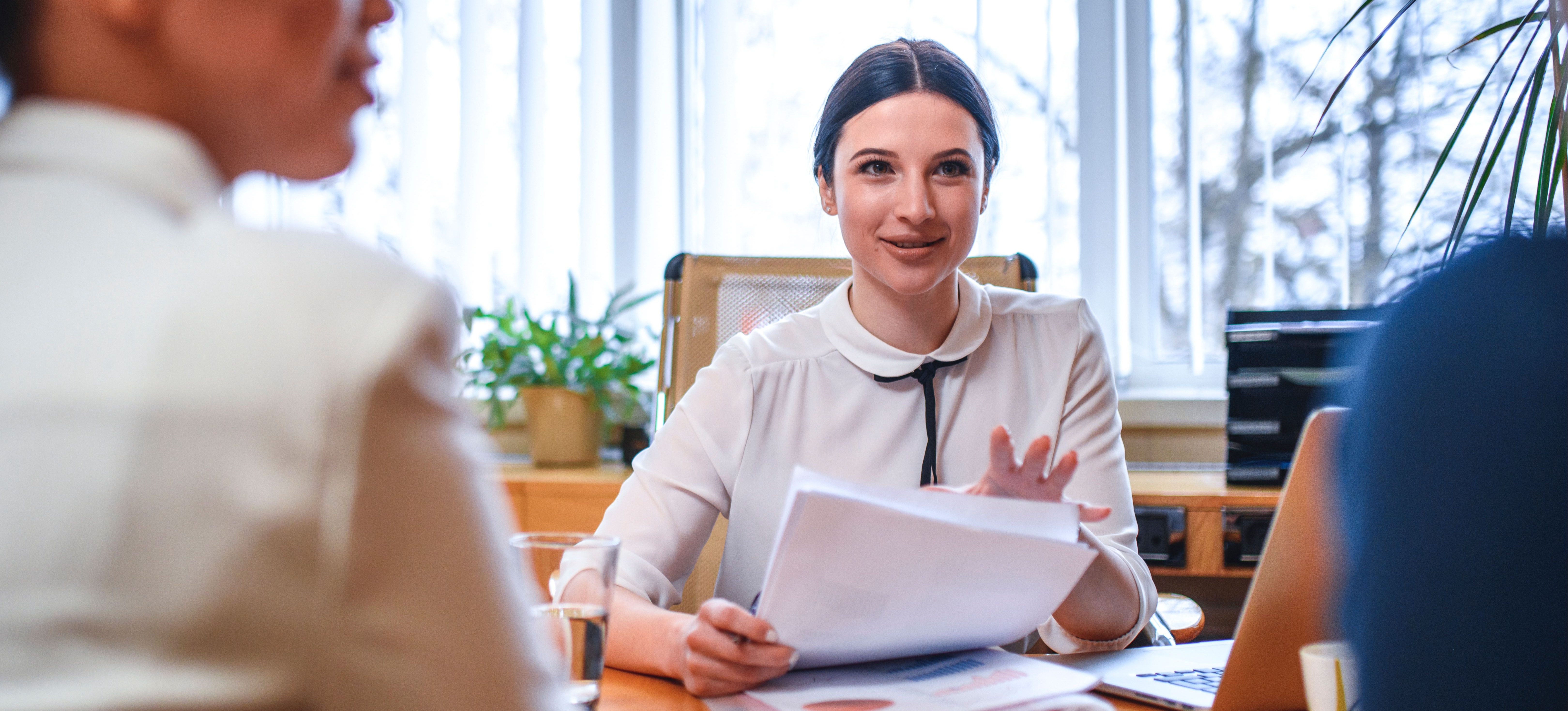[Featured Image] An HR professional is holding pieces of paper and conducting an interview.  They are talking to two potential candidates.
