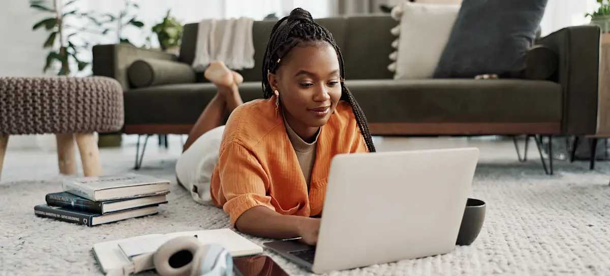 [Featured Image] A learner with books and headphones lies on their living room floor in front of a laptop and uses ChatGPT prompts for learning.