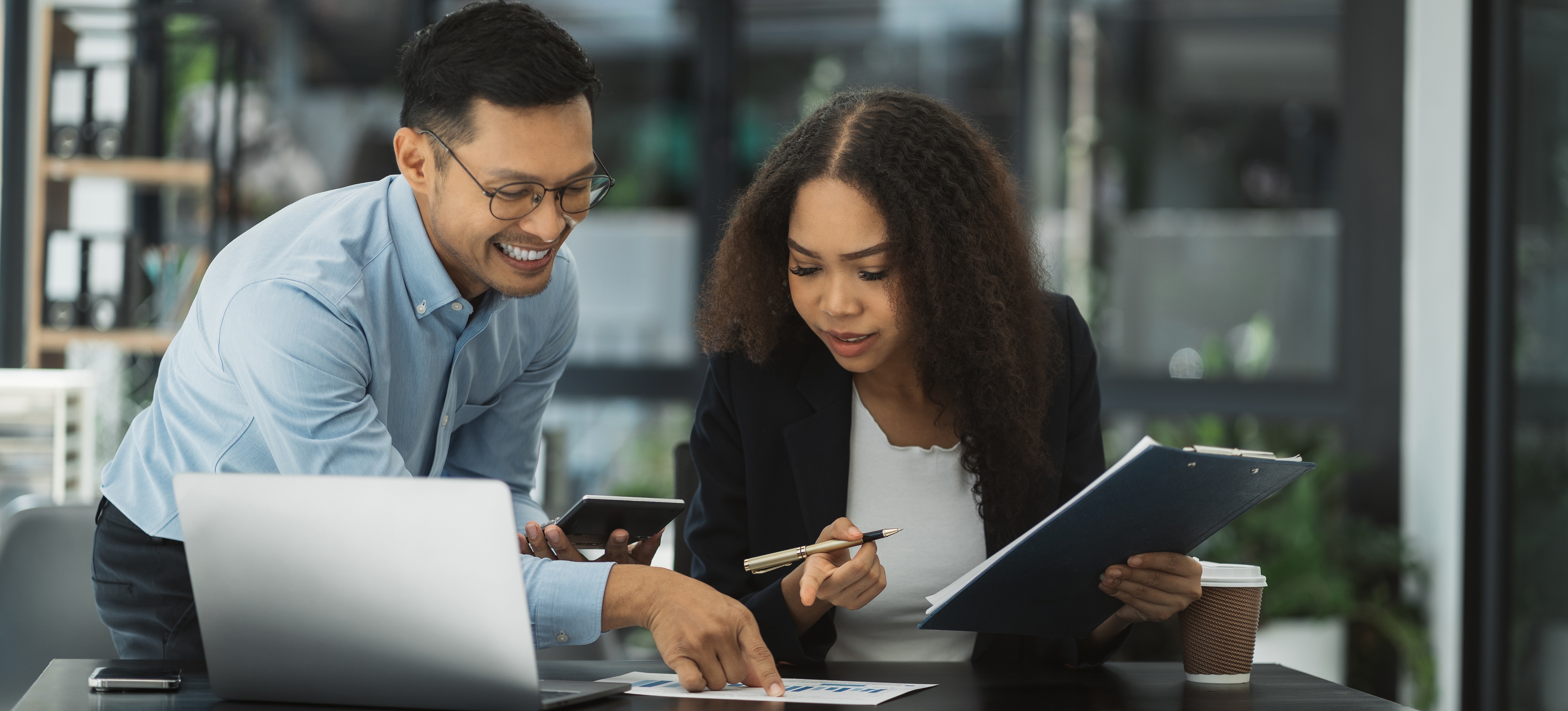 [Featured Image] A business manager demonstrates how to calculate ROI to a colleague.