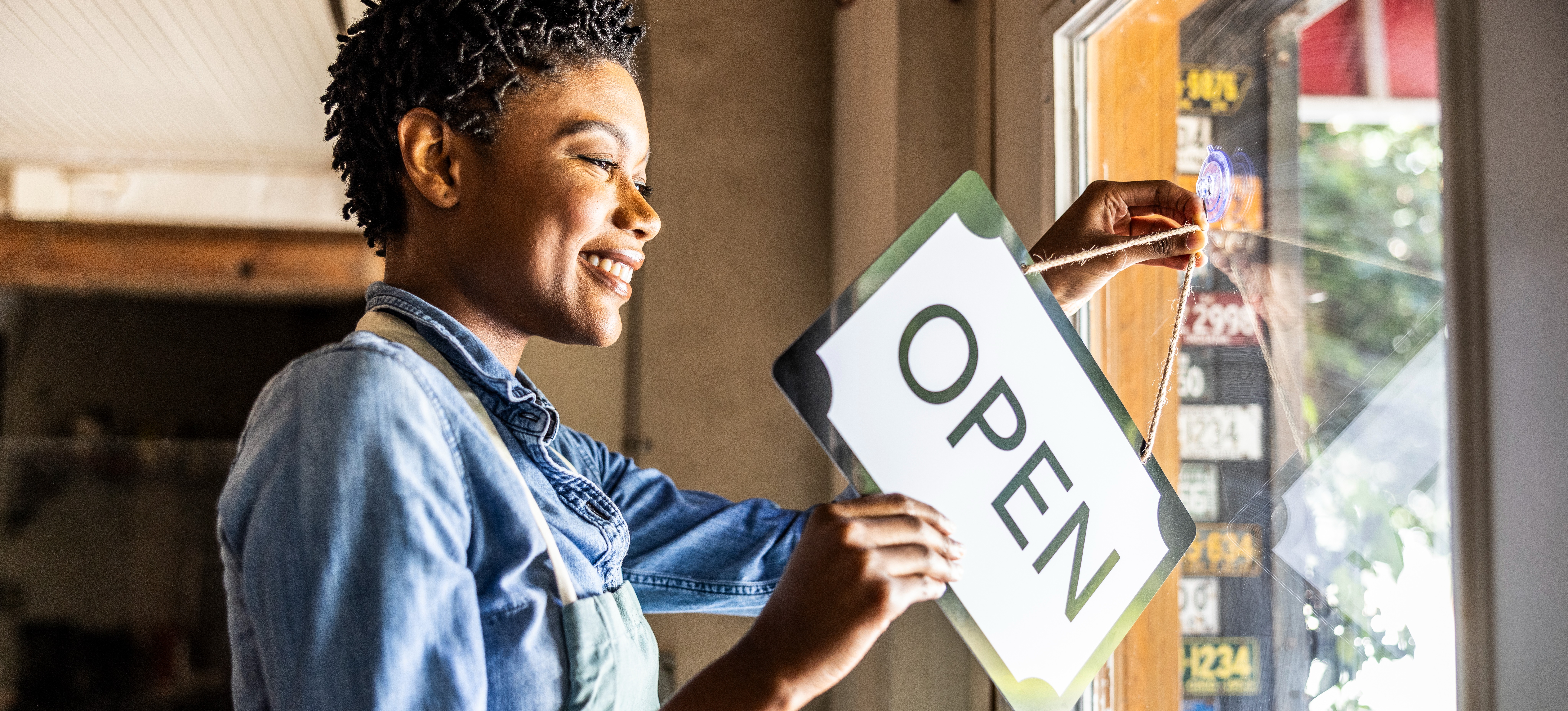 [Featured Image] A small business owner with SBE certification places an open sign in the business window.

