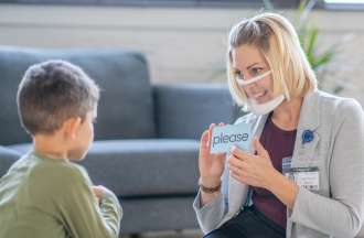 [Featured Image] A blonde, female speech pathologist works with a young male student using flashcards. 
