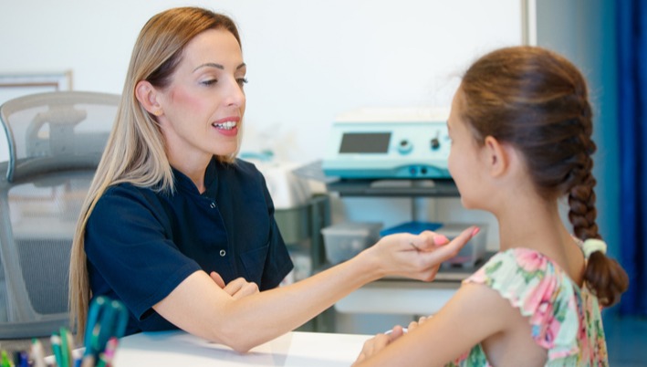[Featured Image] A speech pathologist works with a young student using flashcards. 
