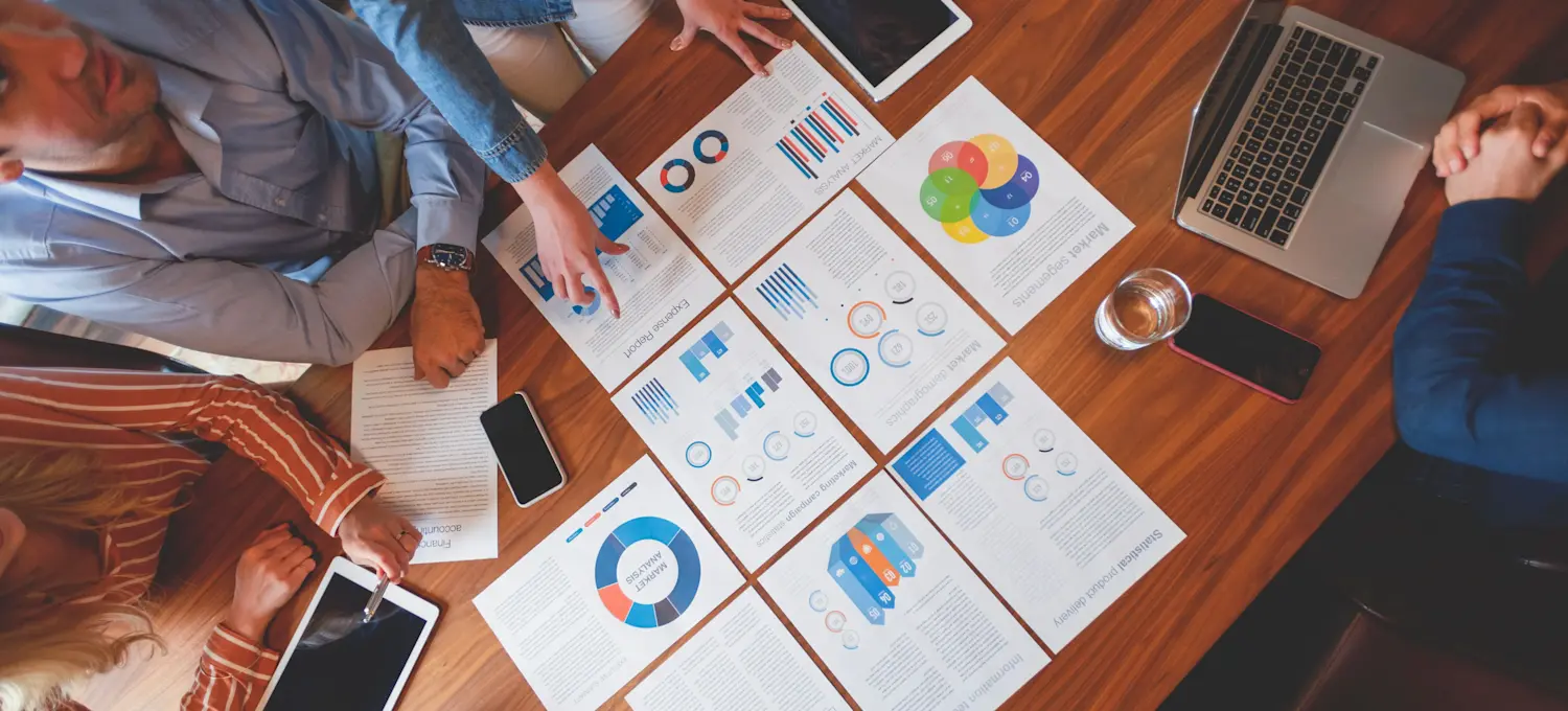 [Featured image] Analysts study sheets of paper containing statistical harts and graphs
