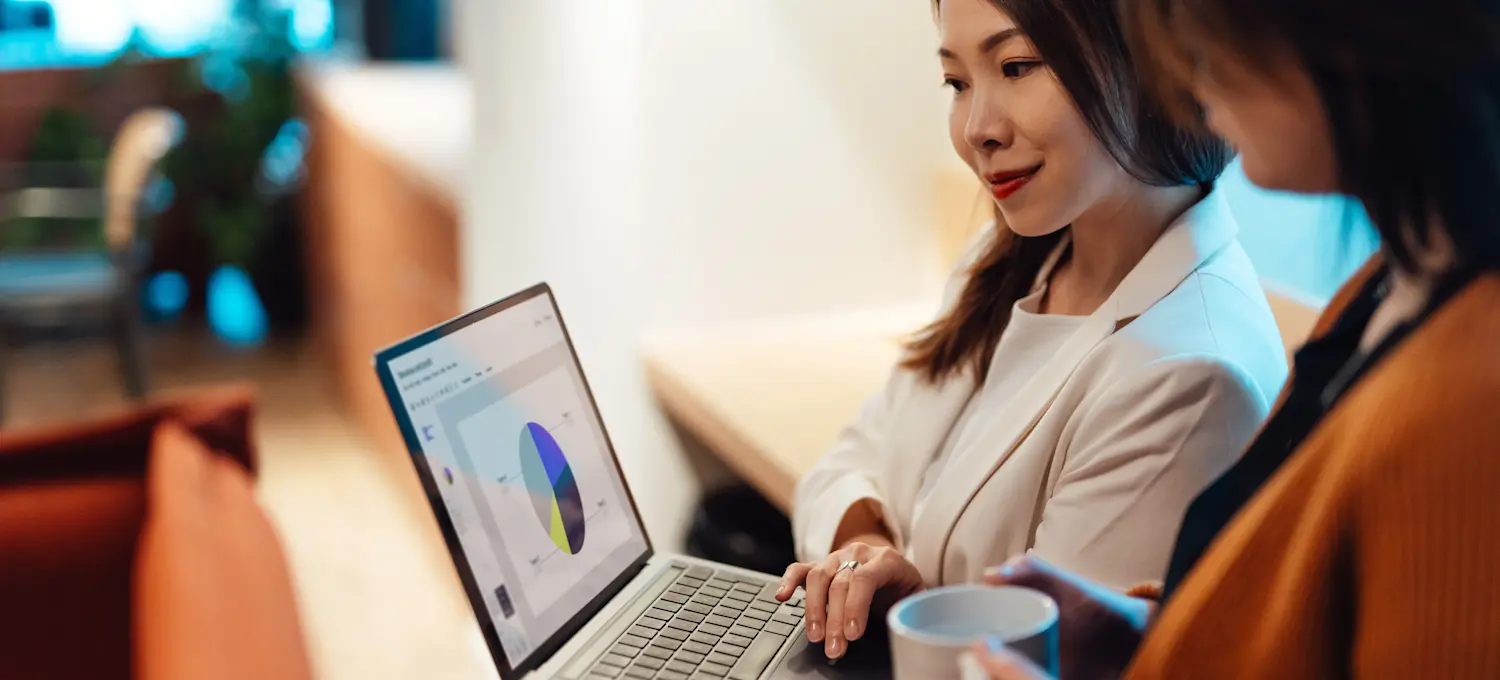 [Featured image] A smiling businesswoman in a white suit holds a laptop displaying a pie graph as she and her colleague stand in an office and discuss big data vs. small data.
