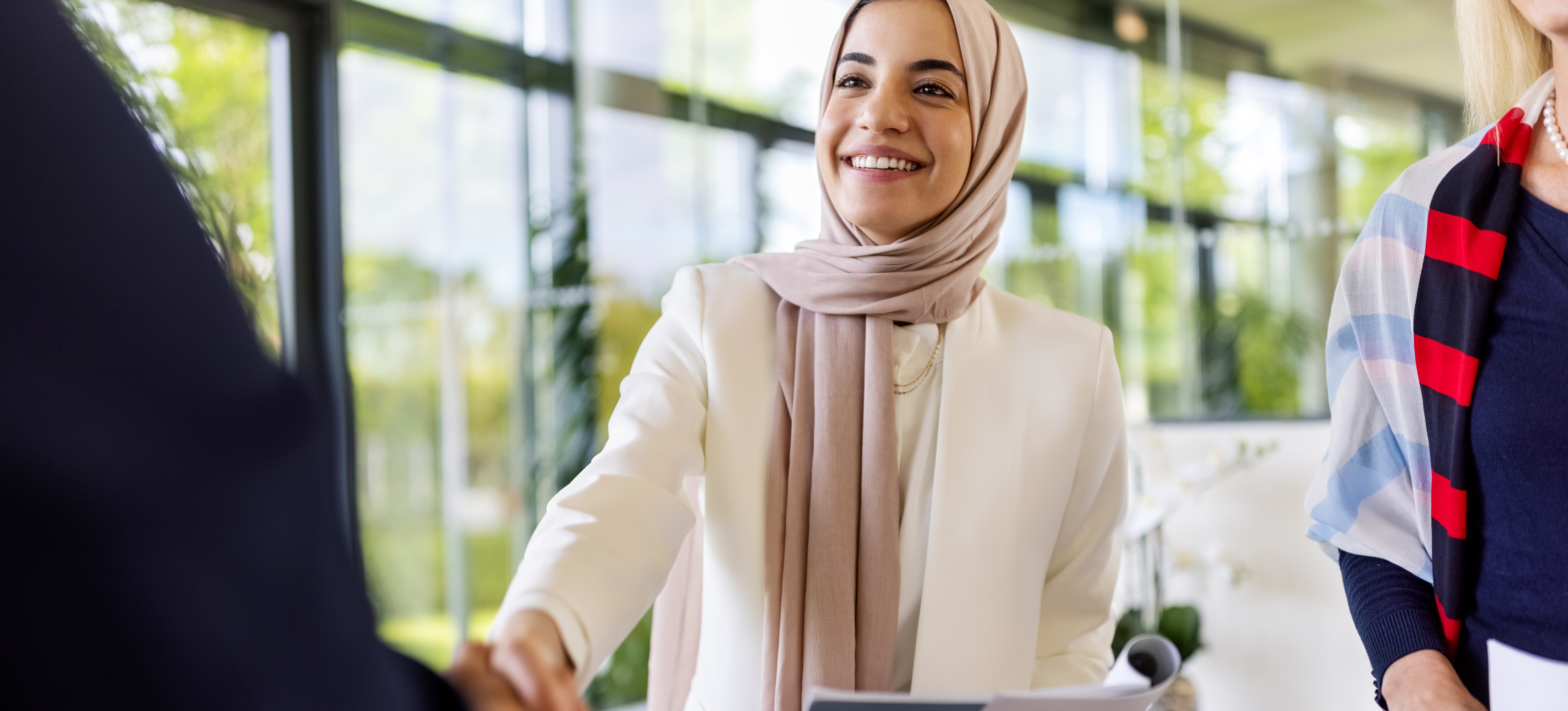 [Featured Image] A smiling job candidate who has expressed her salary expectations in an interview shakes the hand of the potential employee who has been conducting the interview with their colleague.
