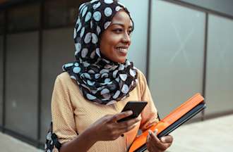 [Featured image] A Master of Public Health (MPH) student walks through a college campus with her cellphone and a stack of notebooks.