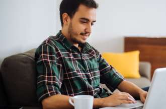 [Featued image] A person in a green plaid button-down shirt sits in a chair and searches for IT jobs on a laptop.