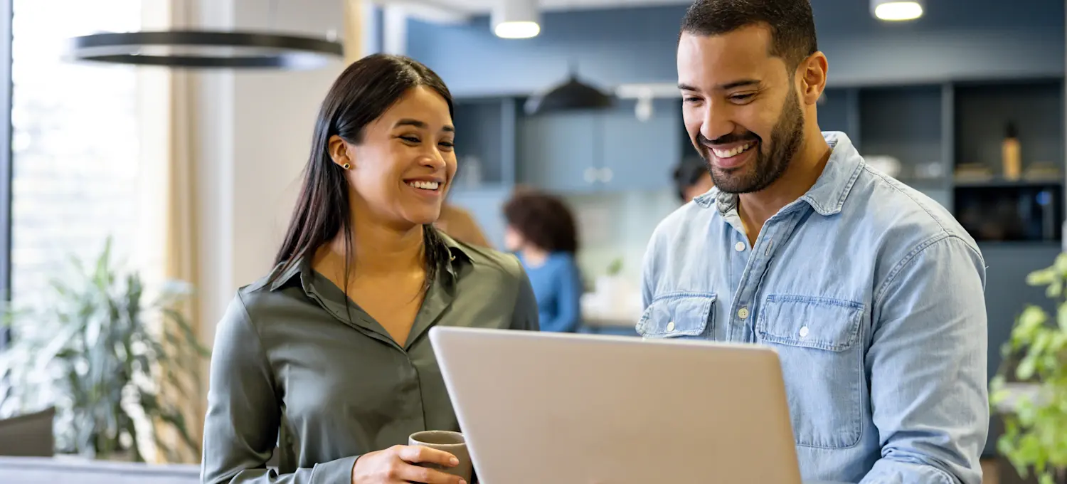[Feature Image]: A smart contract developer shows an employee they’re mentoring part of their development process on a laptop computer while standing in a professional office environment.
