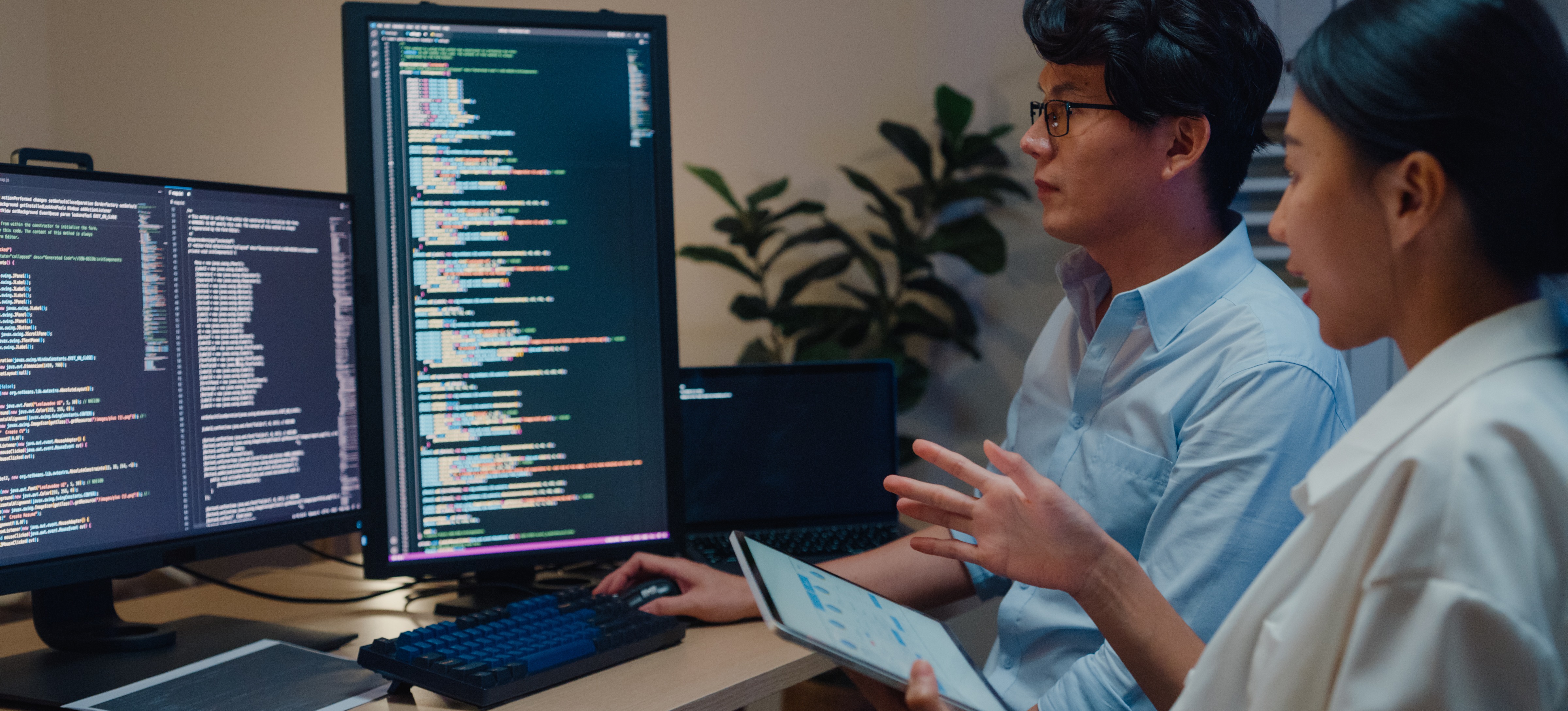 [Featured Image] Cybersecurity specialists in a professional environment, analyzing security-related code on their computer and interacting about the topic.
