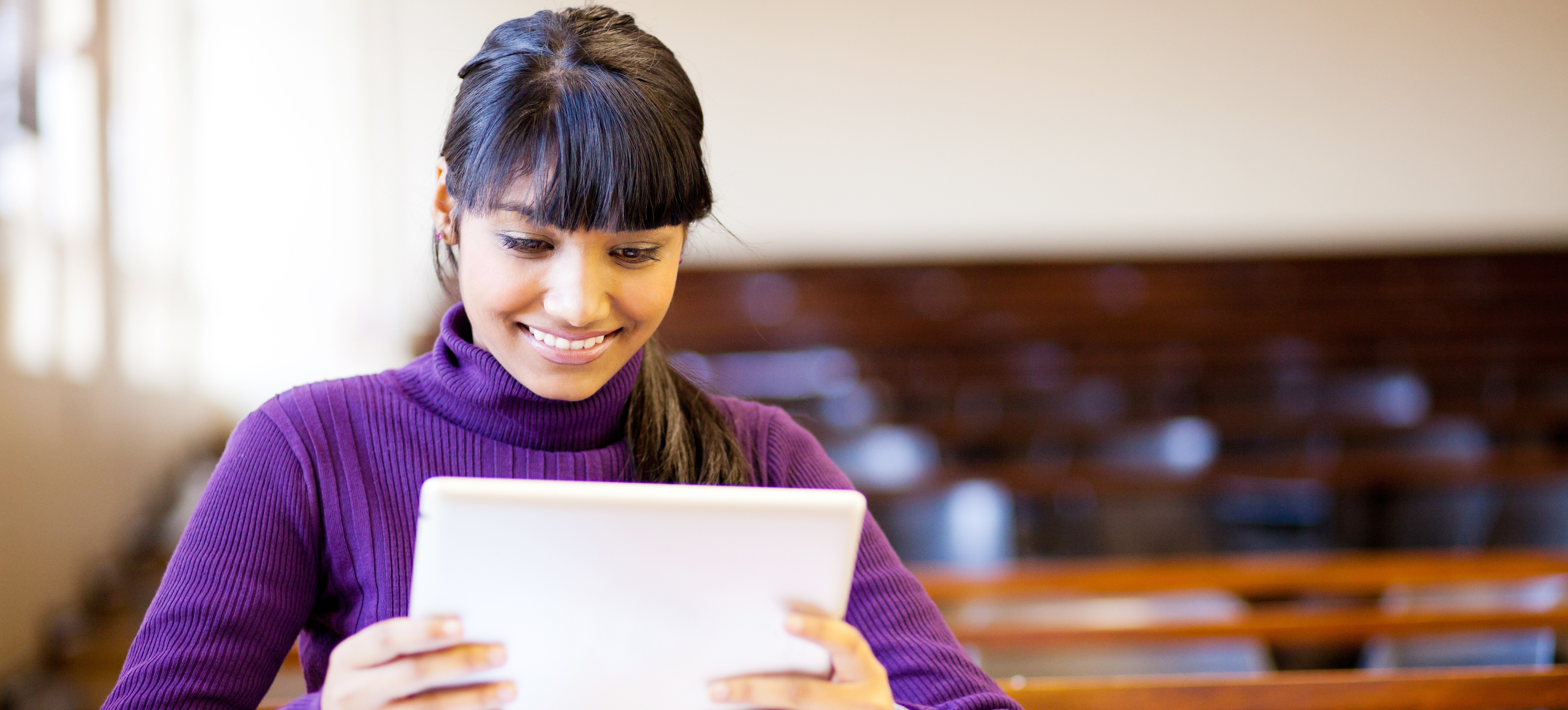 [Featured Image] A university student sits inside a classroom and uses a tablet to study for a course while earning her BTech in Computer Science. 