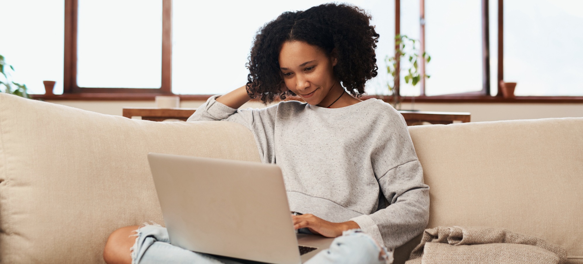 [Featured Image] A young person sits on a couch using their laptop. 