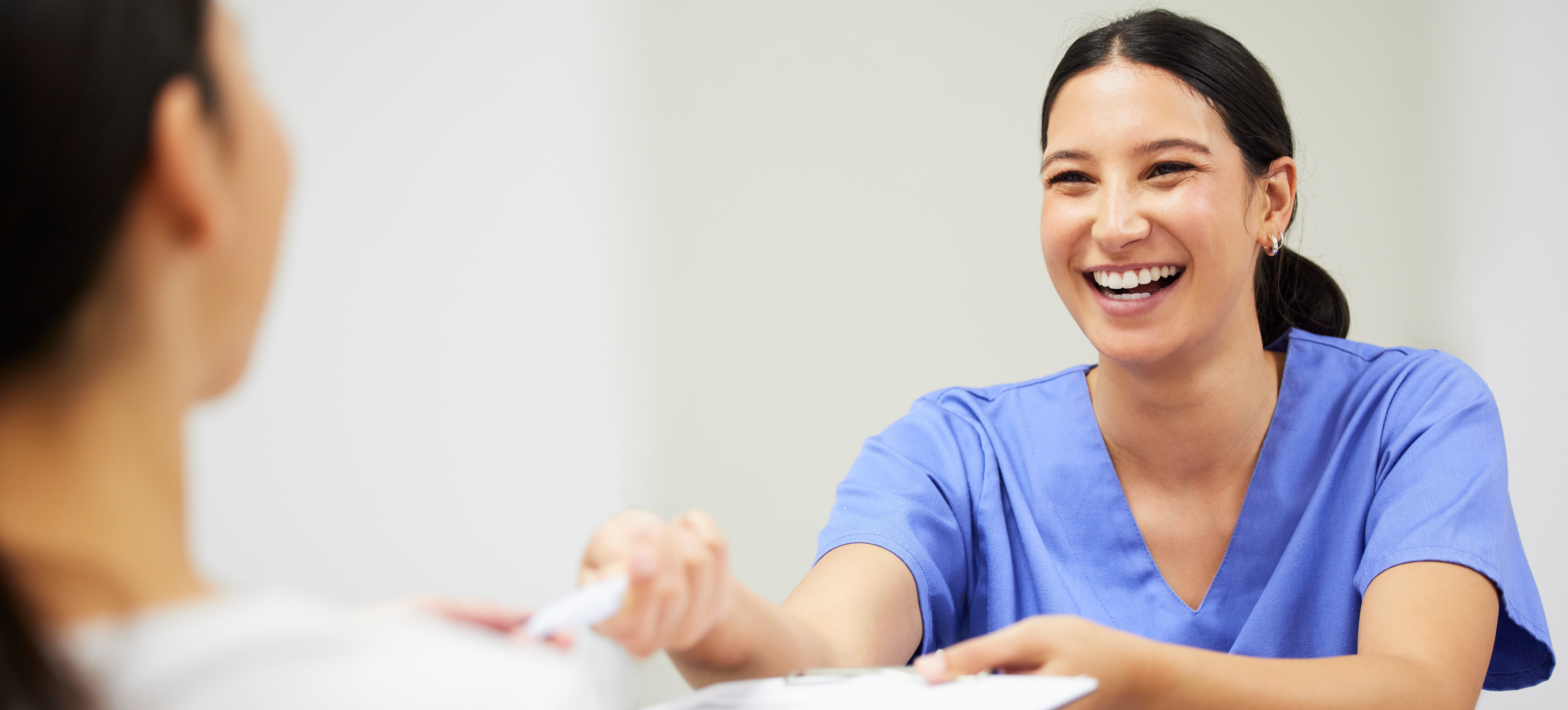 [Feature Image] A registered medical assistant smiles while handing paperwork to a patient. 
