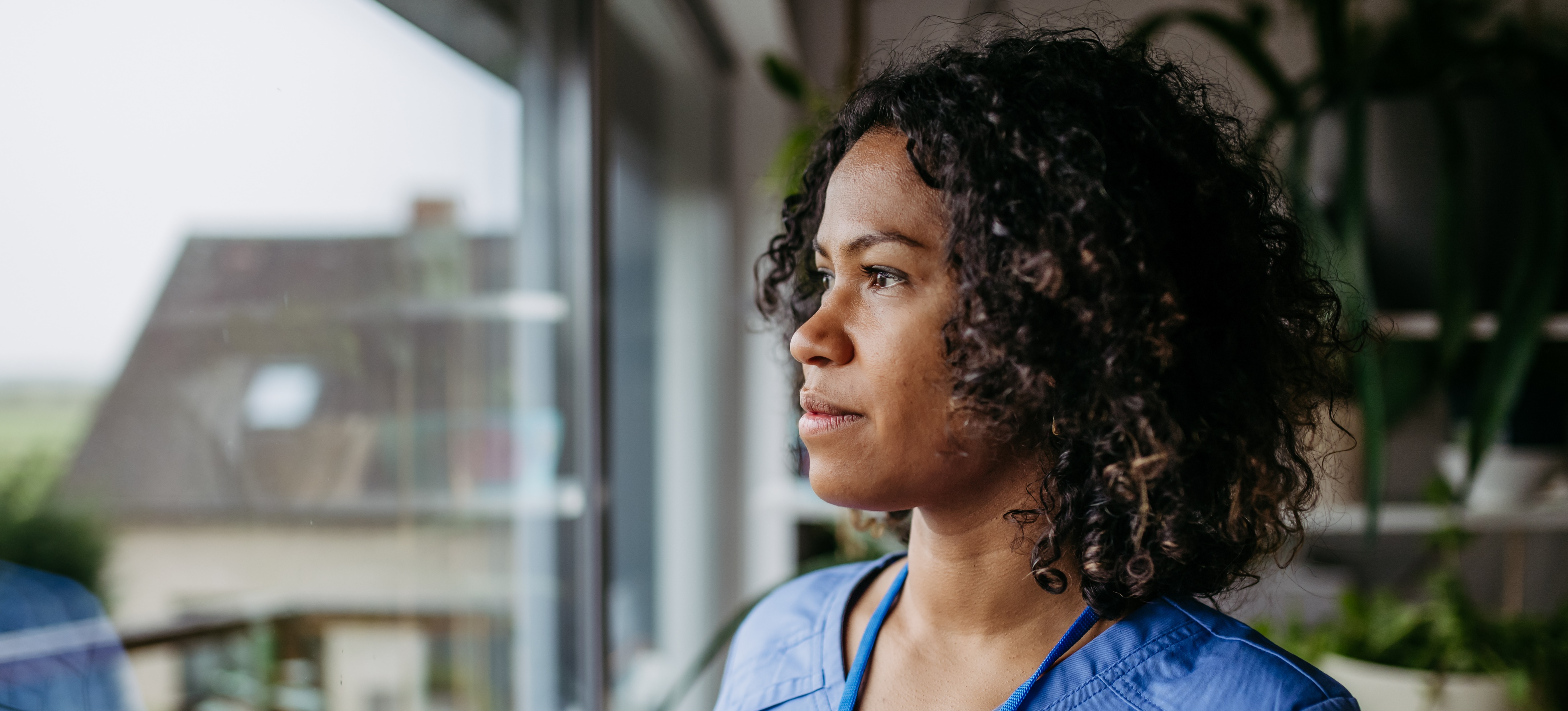 [Featured Image] A nurse looks out the window while thinking about professional nursing goals.

