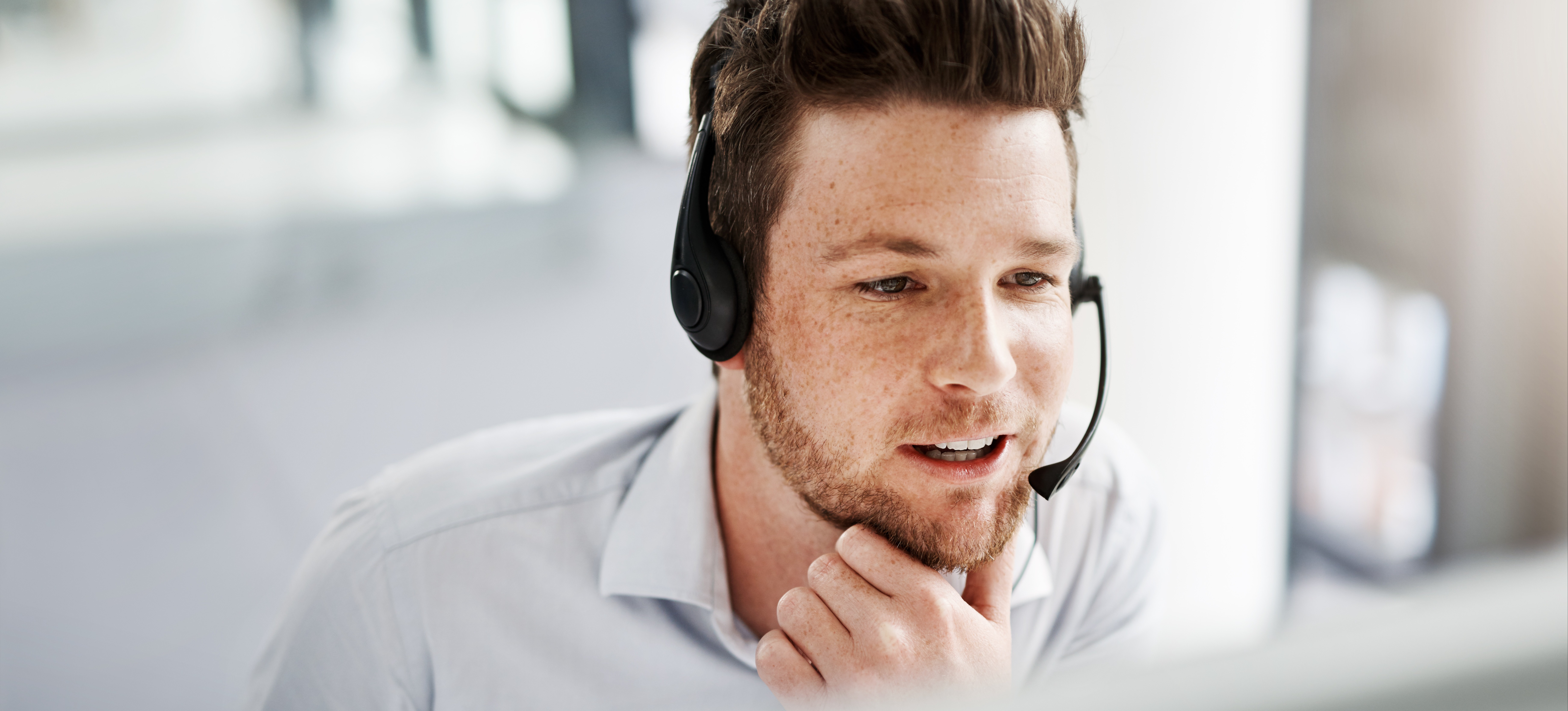 [Hauptbild] Ein Mitarbeiter, der für die Gehaltsstufe eines Vertriebsentwicklungsvertreters arbeitet, spricht über ein Headset mit einem potenziellen Kunden am Telefon, während er auf seinen Computer schaut.