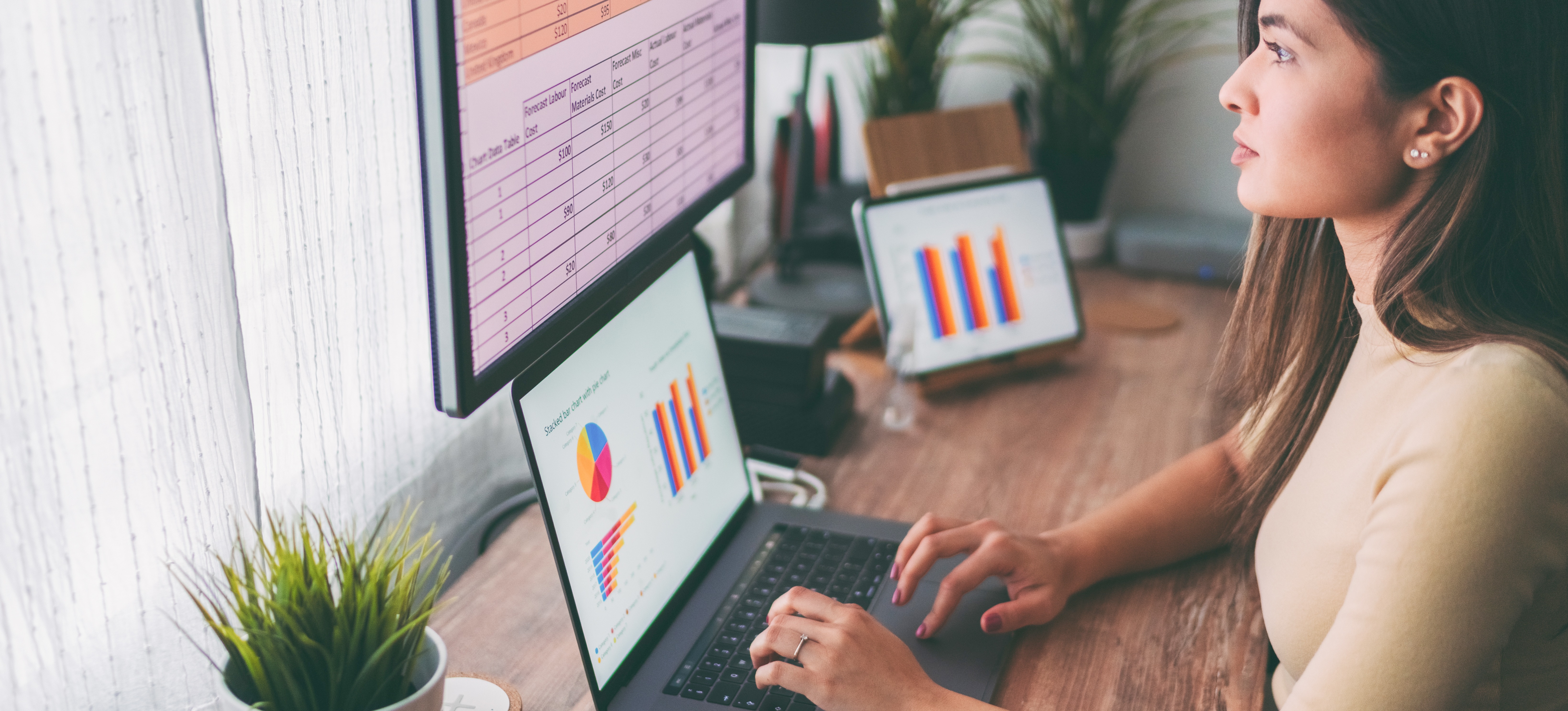 [Featured Image] An operations analyst sits at their desk in front of a window and works with graphs and data on three computer screens.
