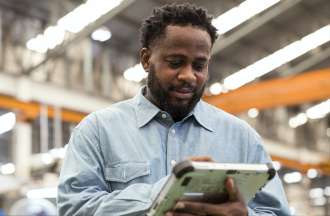 [Featured Image] A male African-American engineering manager using a digital tablet in the production line in a manufacturing plant