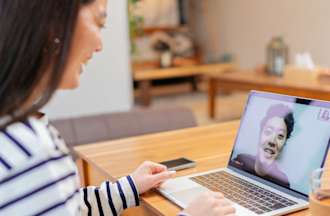 A customer service representative in a blue and white striped shirt speaks with a customer on her laptop.