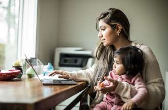 [Featured image] A mother holds her baby on her lap as she uses generative AI on her laptop to make a list of fun games to play with her child.