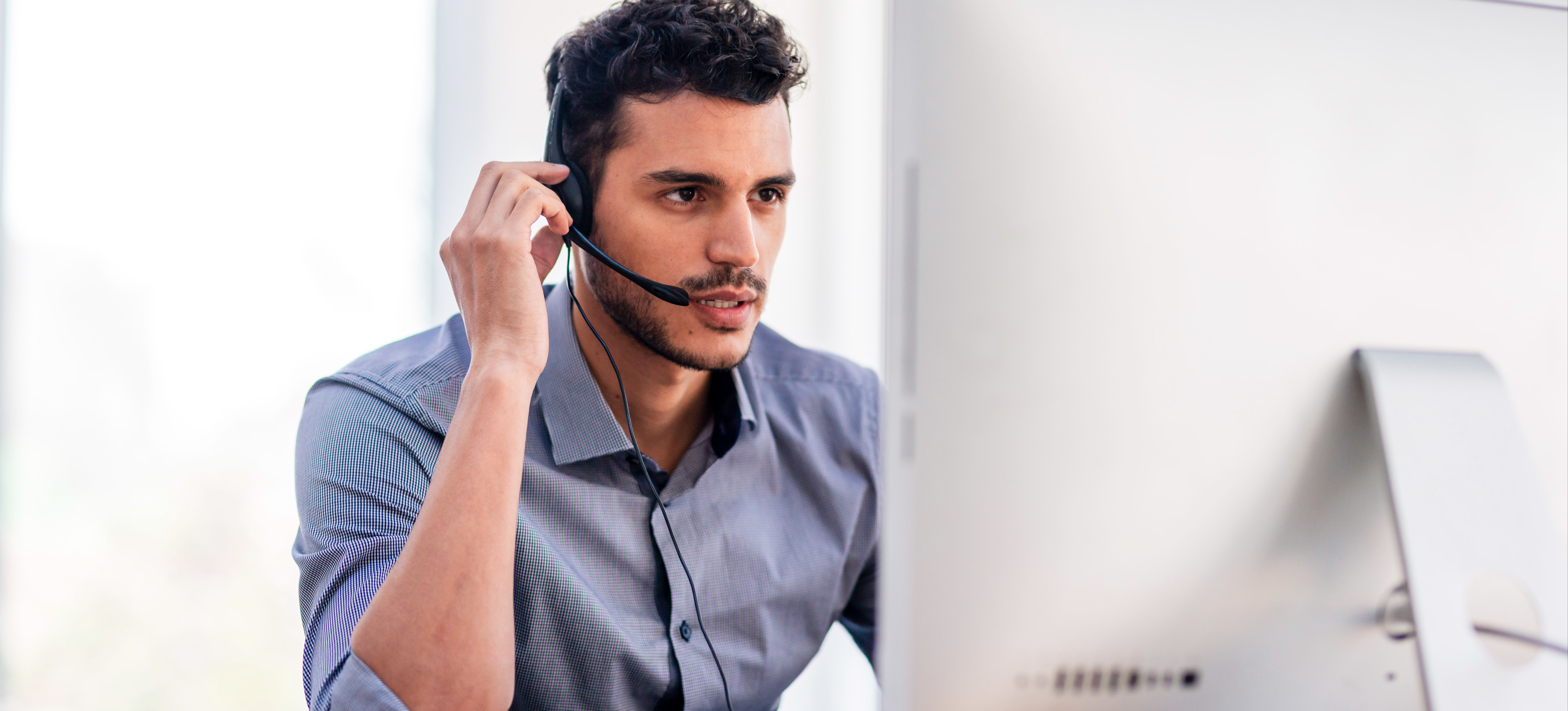 [FEATURED IMAGE] A computer support specialist wearing a headset looks ahead at a desktop computer screen.
