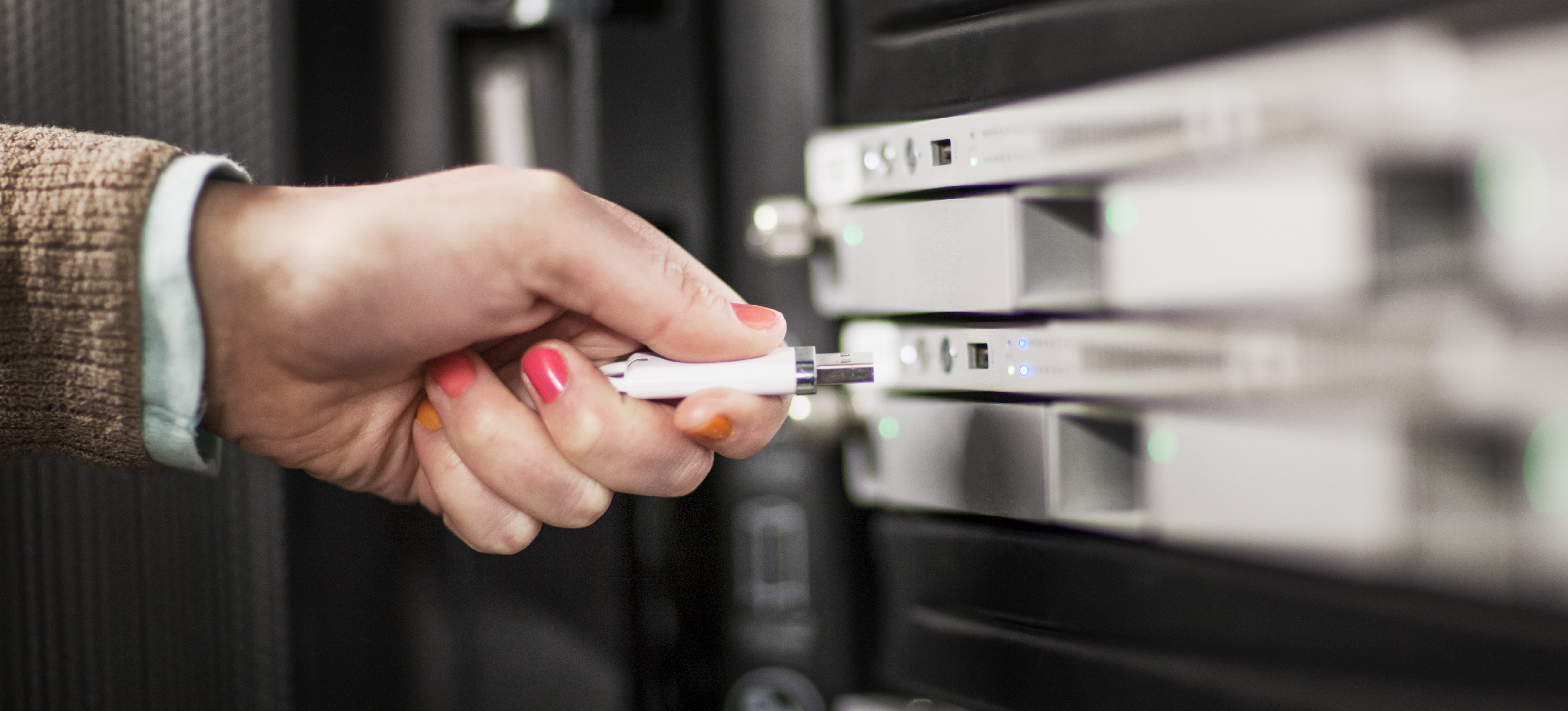 [Featured Image] The hand of a computer programmer is inserting a thumb drive into the computer to upload and get into Linux.
