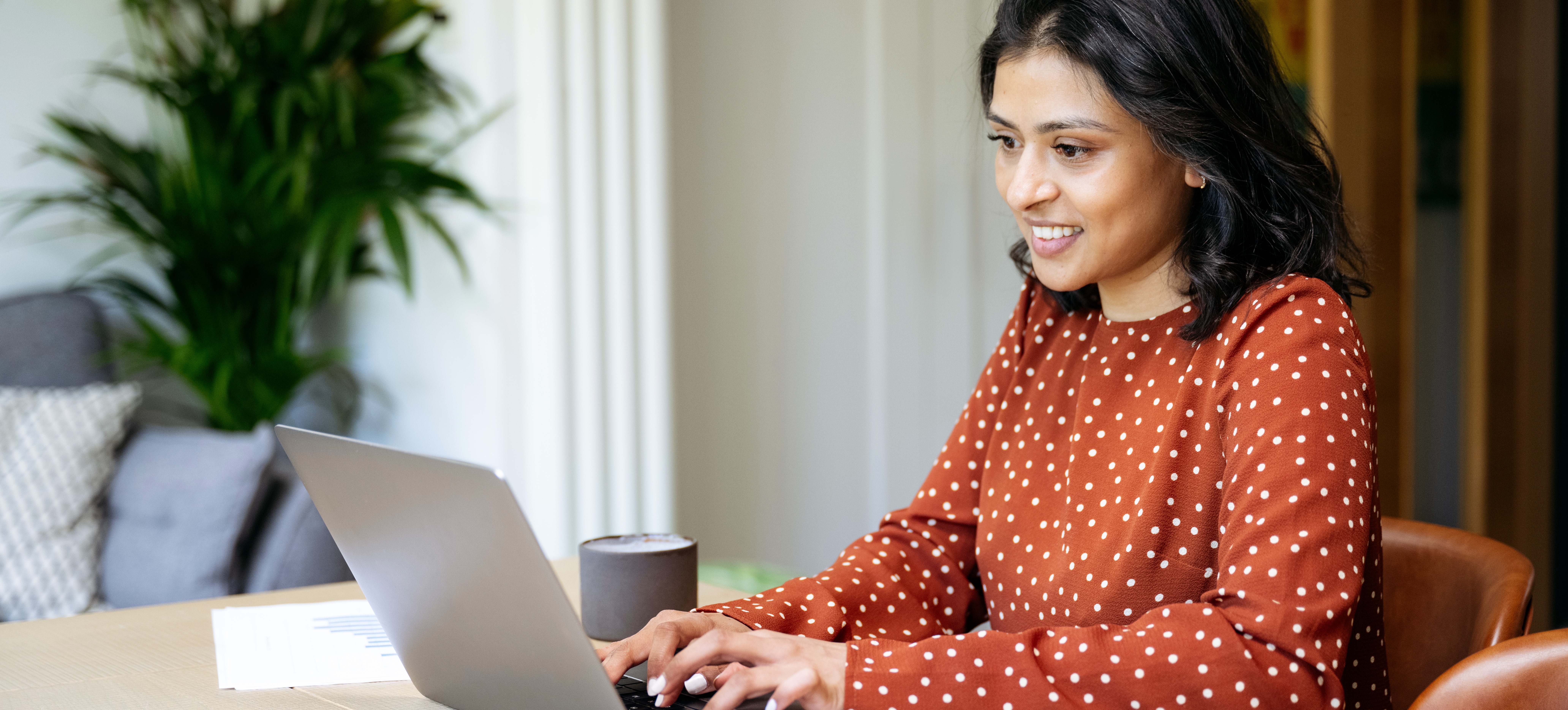 [Featured Image] A smiling woman in a red dress sits at her work computer and participates in employee development.