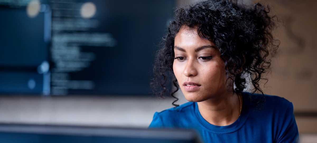 [FEATURED IMAGE] A computer programmer stares at a desktop computer screen in an office.
