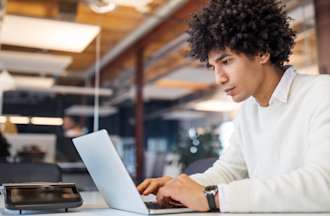 [Featured image] A systems administrator in a white sweater reviews Linux interview questions on his laptop in a co-working space.