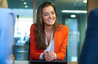 [Featured image] A person in a red blazer sits across a conference table from two interviewers who are asking Azure DevOps interview questions.