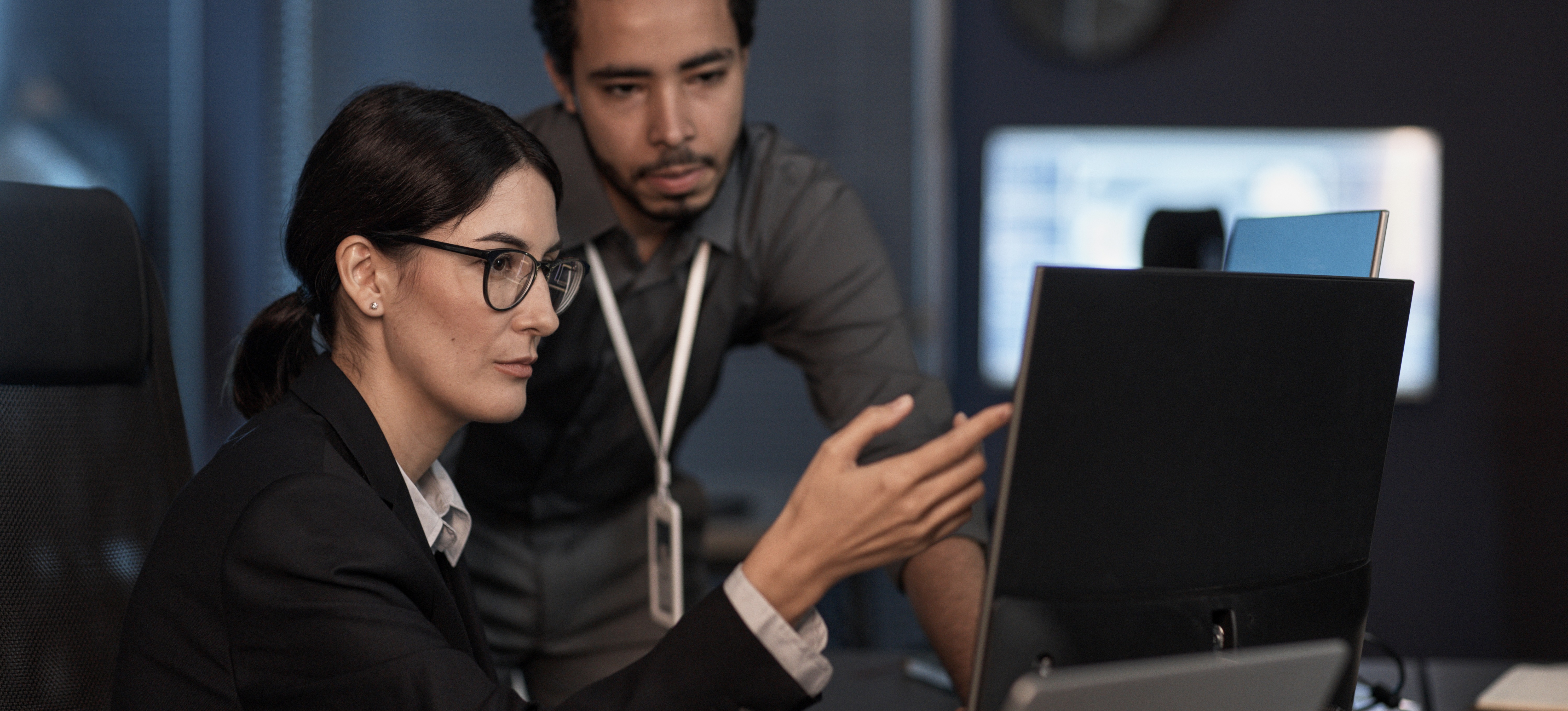 [Featured image] A cybersecurity analyst consults with a colleague while pointing at a computer monitor.
