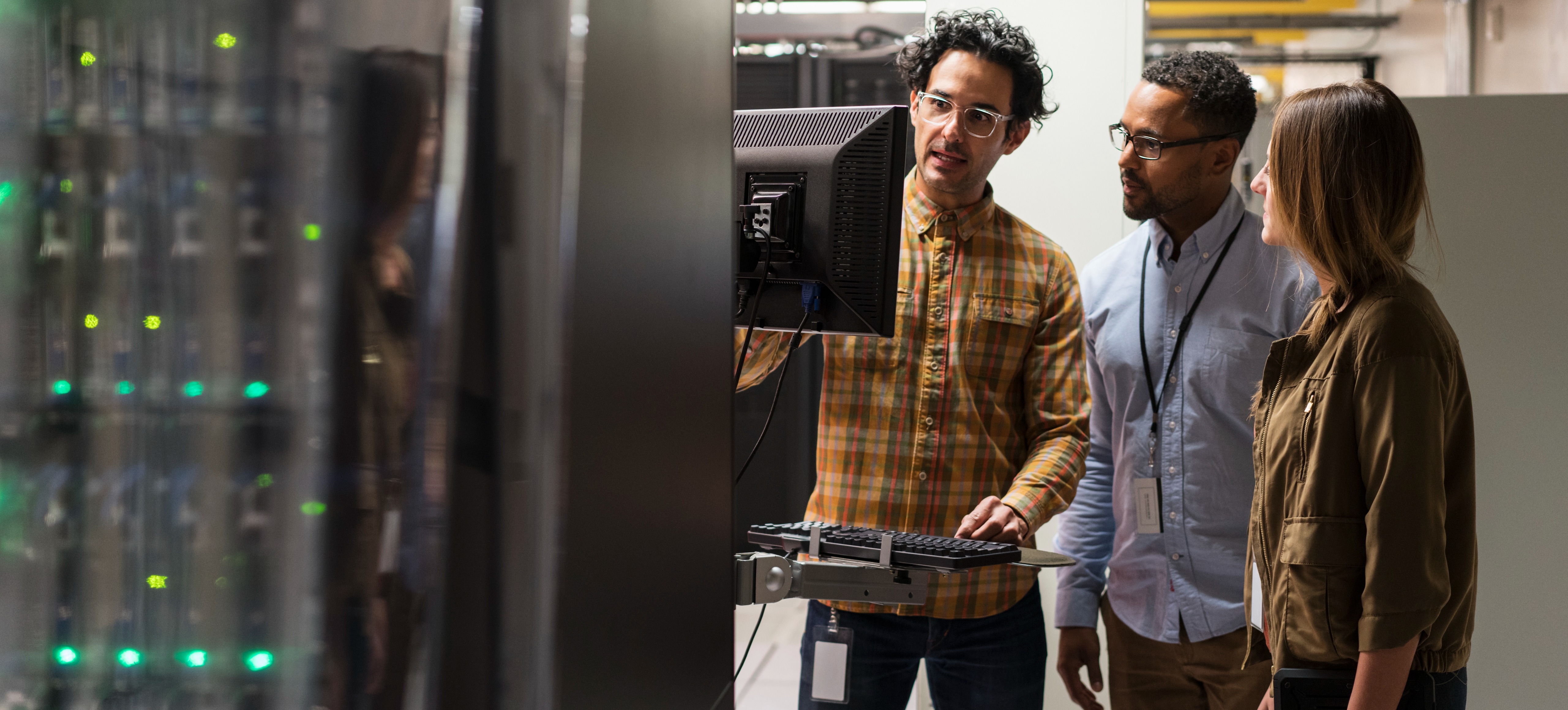 [Featured image] Three people stand around a computer in a server room.