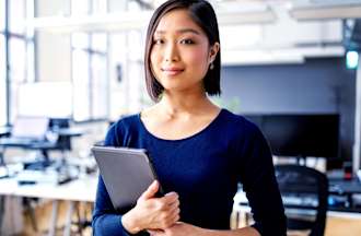 [Featured image] An IT support specialist stands in a brightly lit office holding a tablet.