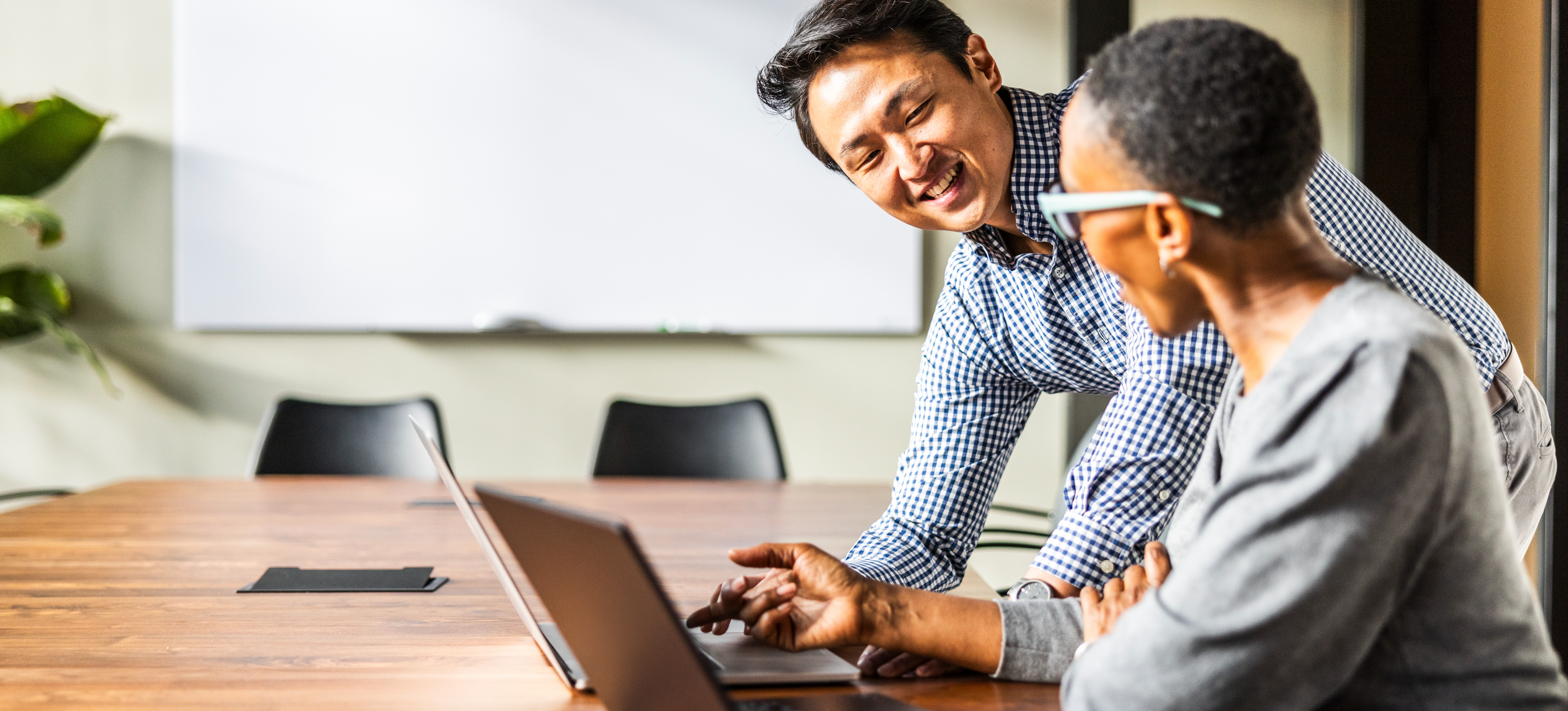 [Feature Image] A developer learns how to use GitHub Copilot on their laptop, with help from their mentor as they discuss its benefits in an empty conference room. 

