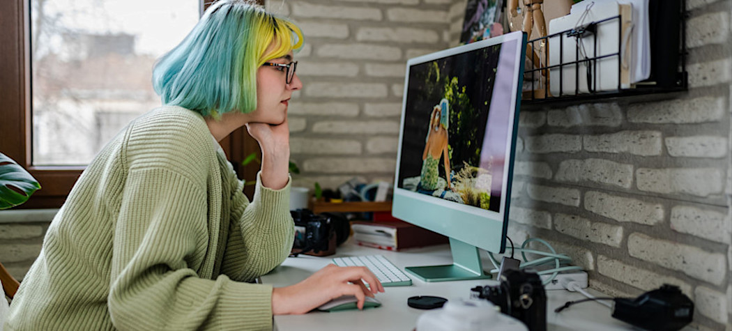 [Featured Image] A person sits at a computer in their home office and uses AI to create videos.